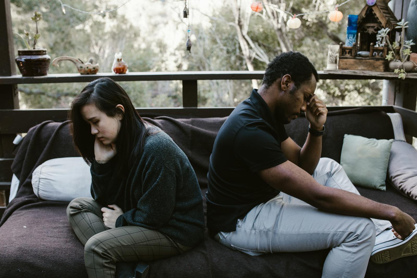 Man and woman sitting back-to-back on a couch, heads down and emotionally distant in a relationship.